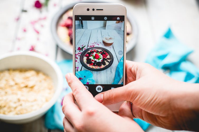 A person uses their smartphone to take a picture of their bowl of porridge.