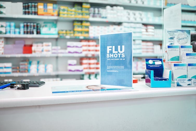 Pharmacy shelves stocked with various products and a sign on a counter advertising that flu shots are available there.