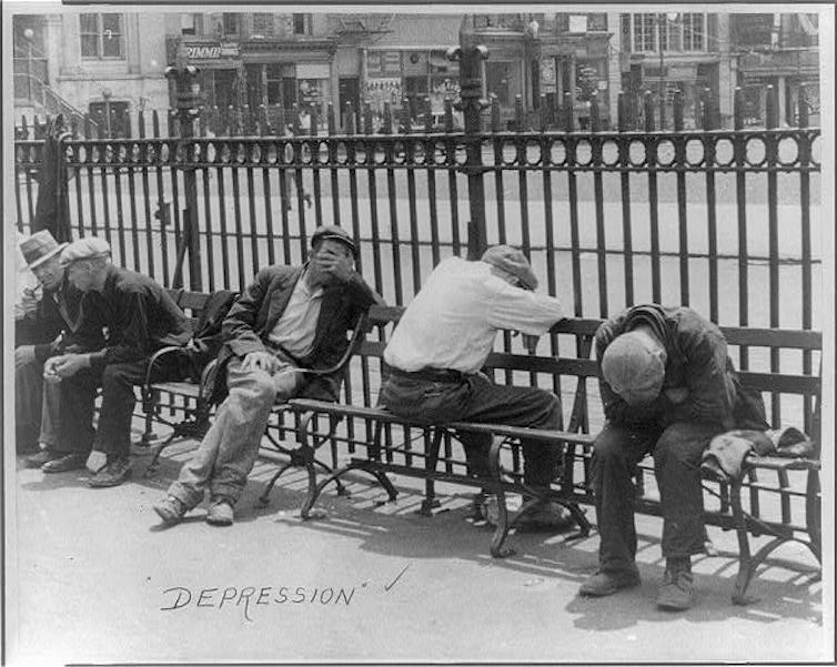 A line of depressed men slumped on a bench in front of a city street