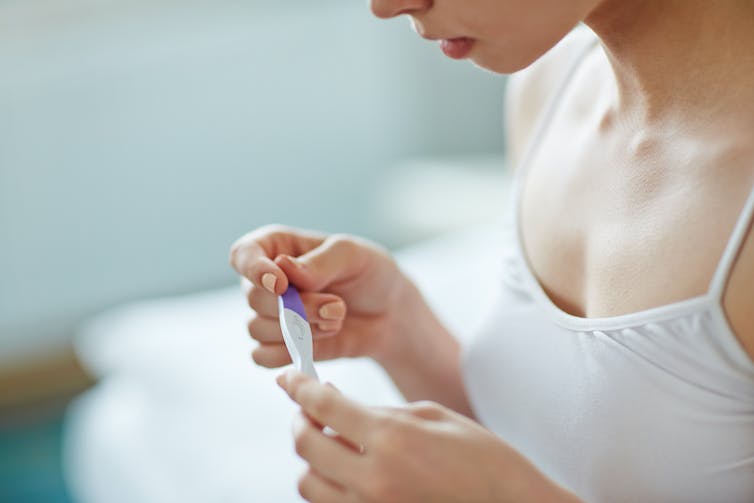 Close up of a woman looking solemnly at a pregnancy test