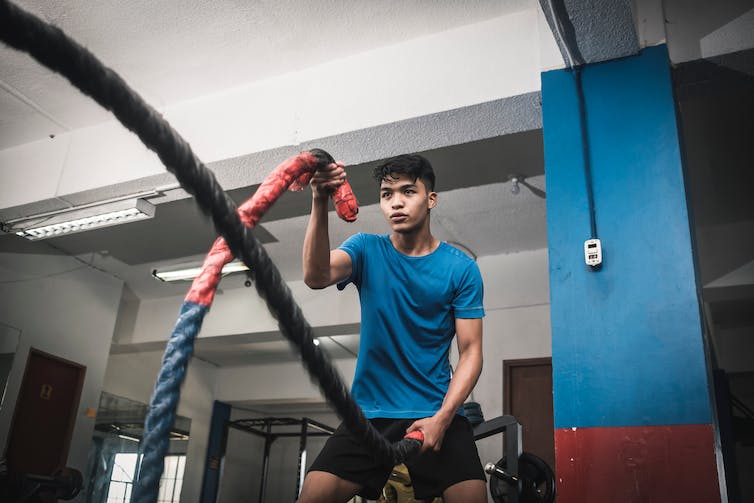 A young man performs an exercise in the gym using battle ropes.