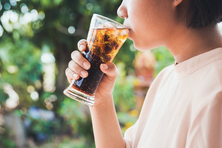 A person drinks a glass of cola.