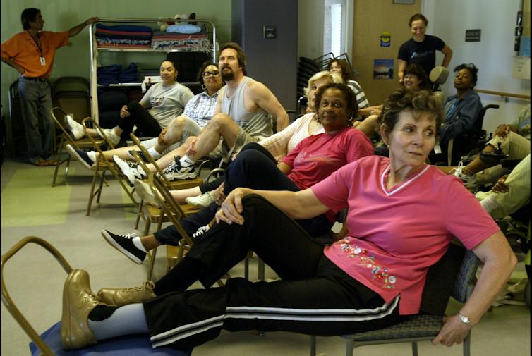 A group of men and women of varying ages, dressed in sportswear, stretch during a yoga class