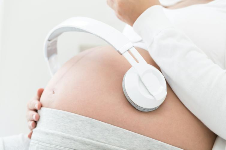 A pregnant woman with headphones on her stomach