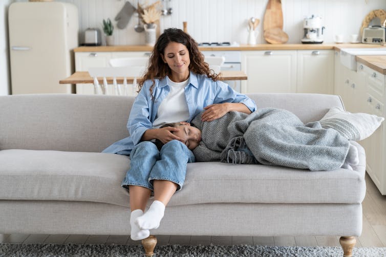 A child wrapped in a blanked on a sofa with head in mother's lap