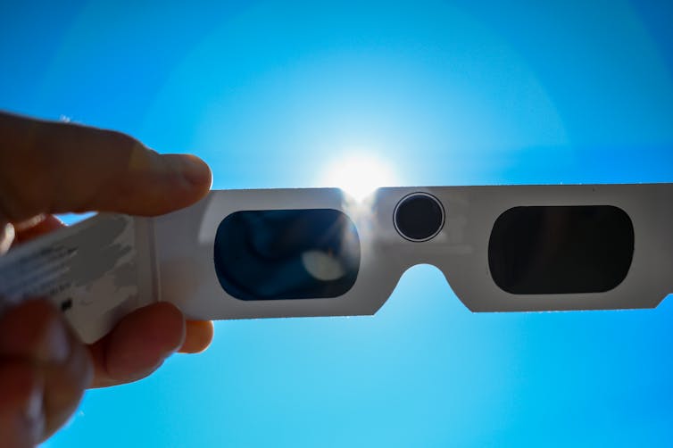 a hand holding solar glasses up to the sun