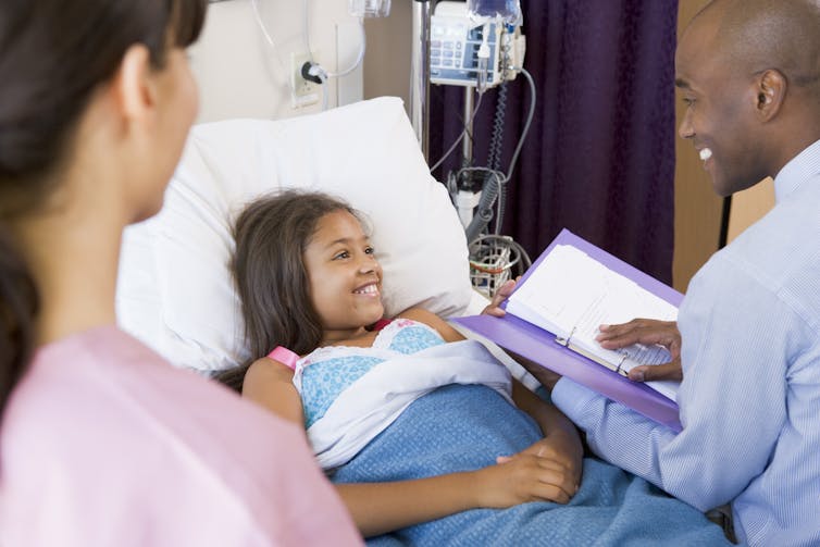 A child in a hospital bed with health-care professional at the edge of the frame