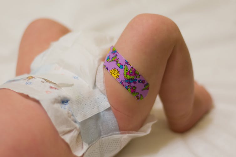 Cropped image of baby ina diaper with a colourful bandage on its thigh