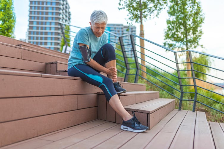 An older woman in running gear holds her shin in pain.