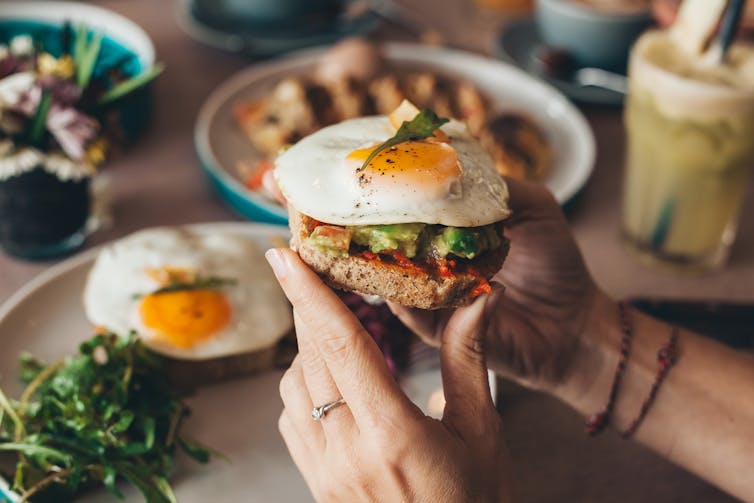 A person holding a piece of toast with eggs and avocado.