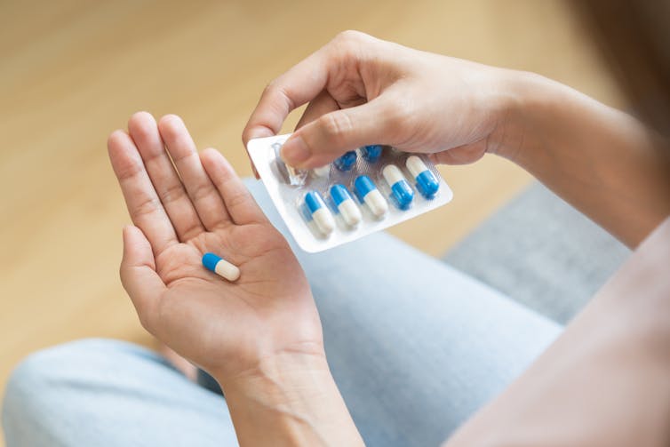 A person holding a blister pack of pills pops one into the palm of their hand.