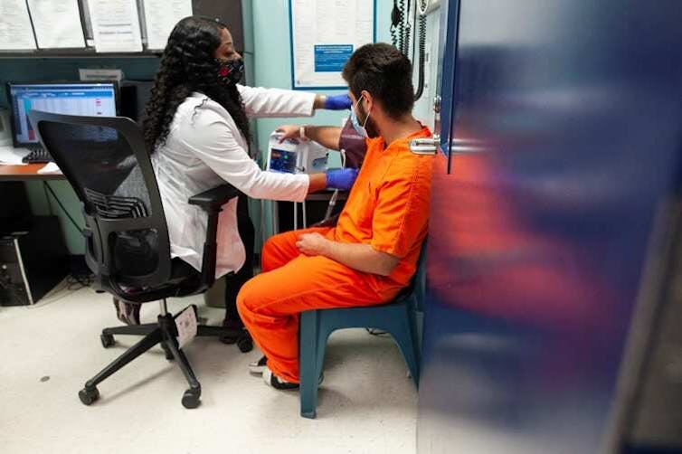 Woman in white coat examines man in orange jumpsuit