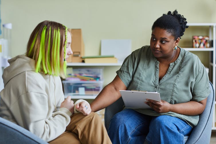 A female school therapist comforts a female teenage patient.