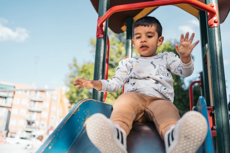 A little boy at the top of a playground slide