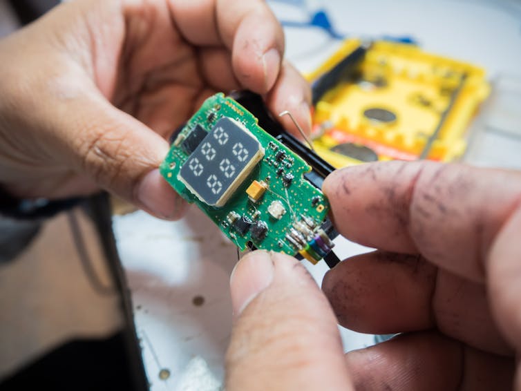 close up of hands holding a small green circuit board