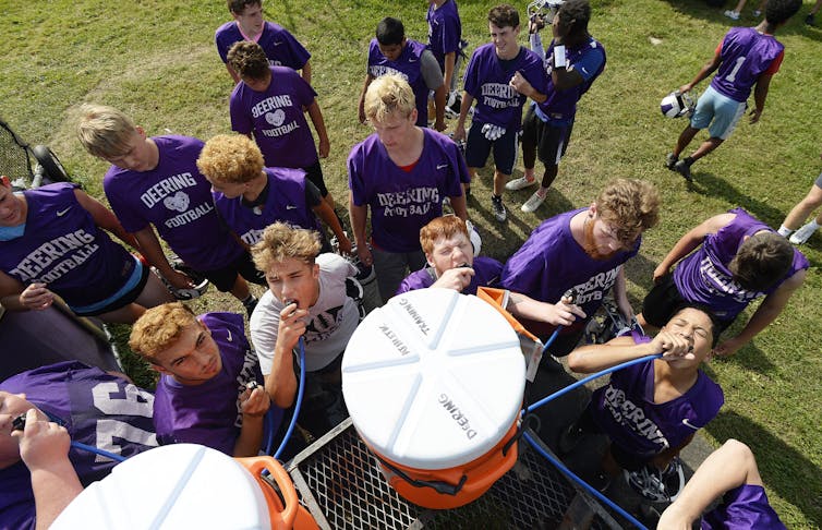 Football teammates, without pads or helmets, take a break around coolers of water on a hot August day.