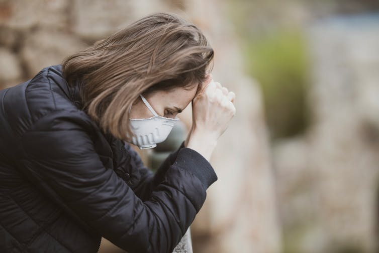 a woman wearing a medical face masks sits with her head in her hands