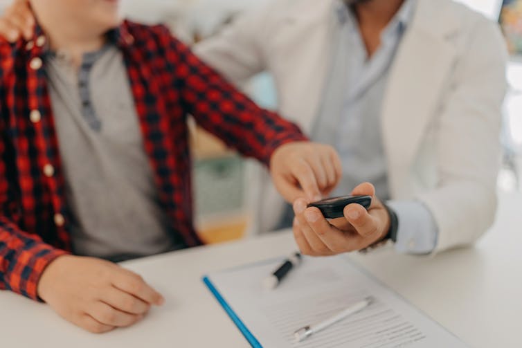 Child measuring blood sugar levels via finger prick on device held by a clinician