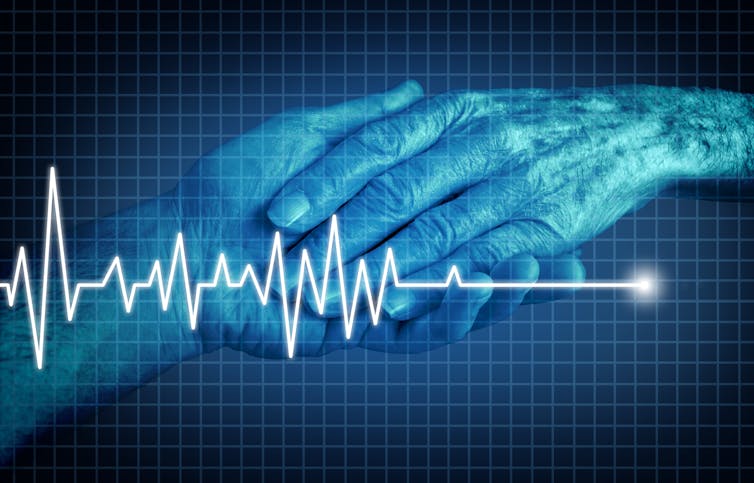 Image of two hands holding each other, overlaid by the trace of a heart monitor.