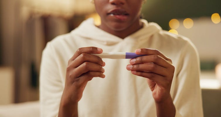 A woman holds a pregnancy test and looks concerned.