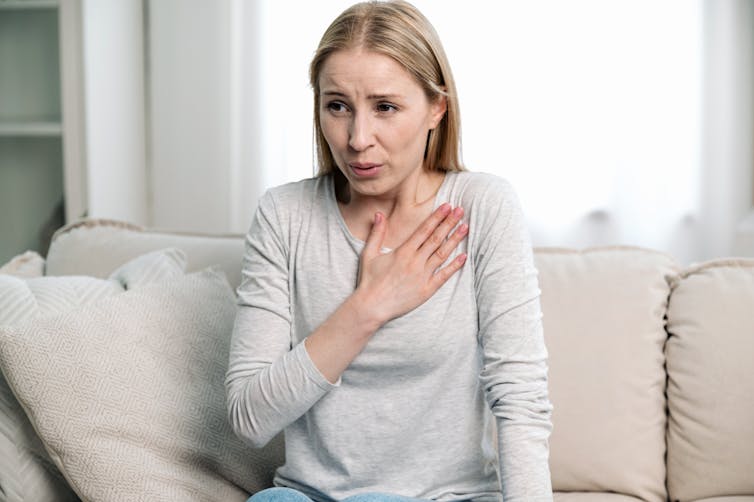 An anxious woman presses a hand to her chest while taking a deep breath.