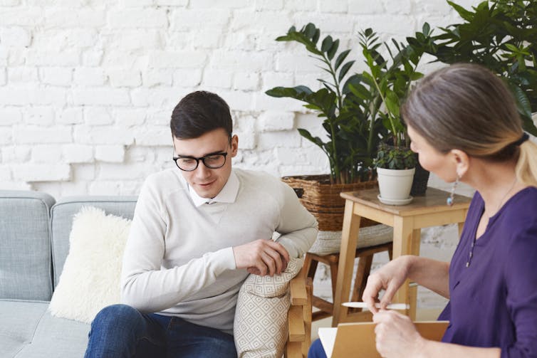 A young man on a couch talks to a woman seated on an adjacent chair