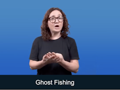 Woman in black T shirt, using hands to create sign language for 'ghost fishing', words in white, blue background