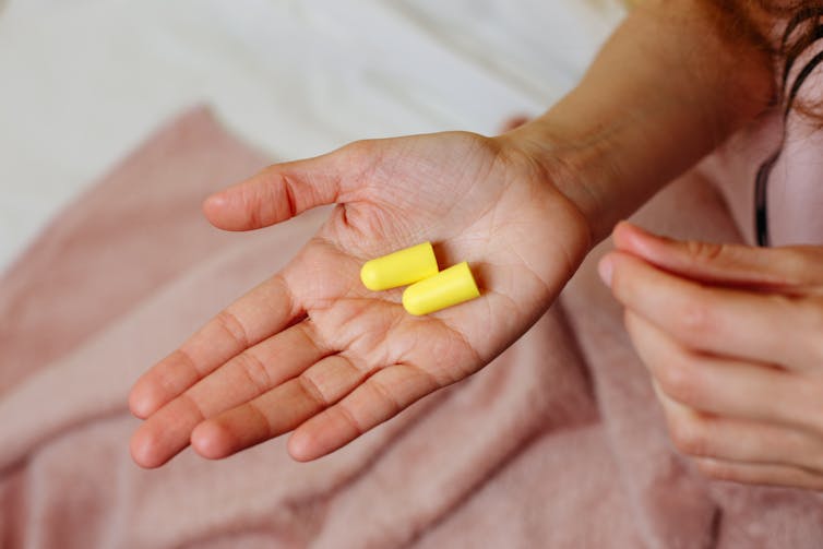 A person holds two foam earplugs in the palm of their hand.