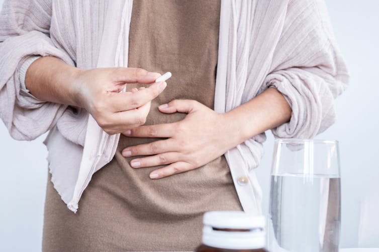 A man holds a probiotic supplement in one hand and presses his stomach with his other hand.