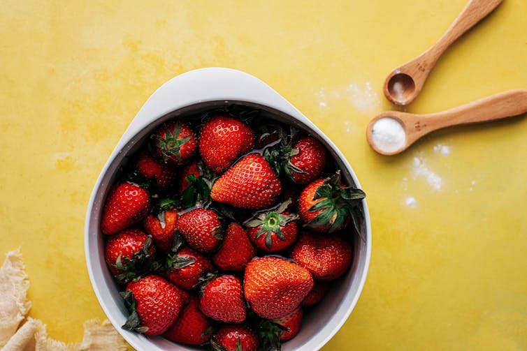 A bowl of strawberries soaking in water, next to a teaspoon of baking soda.