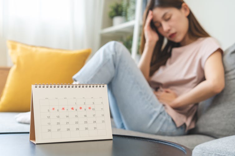 A woman on a sofa with her eyes closed with one hand on her stomach and the other on her forehead, with a calendar in the foreground