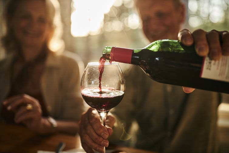 Person pouring wine into glass for another person