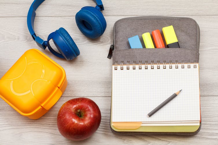 A child's objects organized including a notebook, writing tools and headphones.