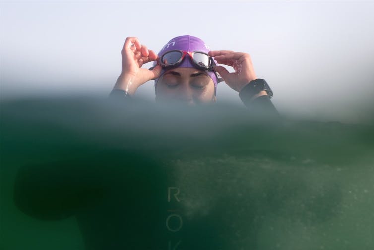 close up of woman in swim hat and goggles, half submerged in blue sea water