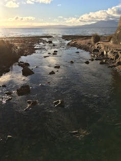 calm water with rocks on either side, looking out to loch, blue cloudy sky