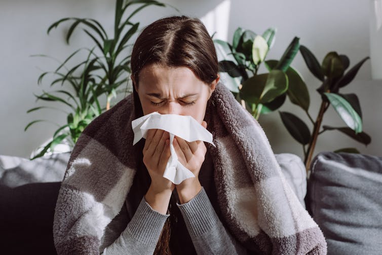 A woman sneezes into a tissue.