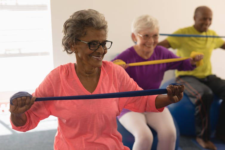 Three older adults taking part in a fitness class with exercise balls and bands