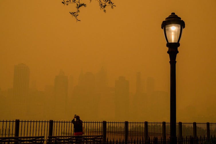 Orange haze blanketing a city skyline, small silhouette of a person taking a photo by a streetlight