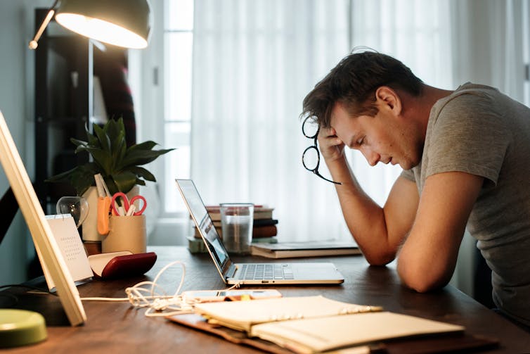 A stressed man sitting at a desk with his hand on his forehead