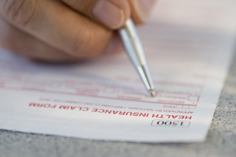 Close-up of hand filling out health insurnace claim form with a pen