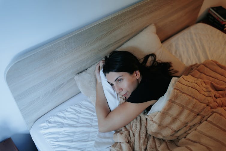 A woman lying on her side in bed looks towards a bright window.