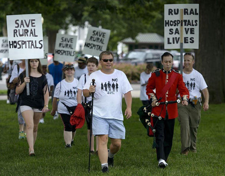 A small group of people march holding handmade signs that read 'Save Rural Hospitals.'