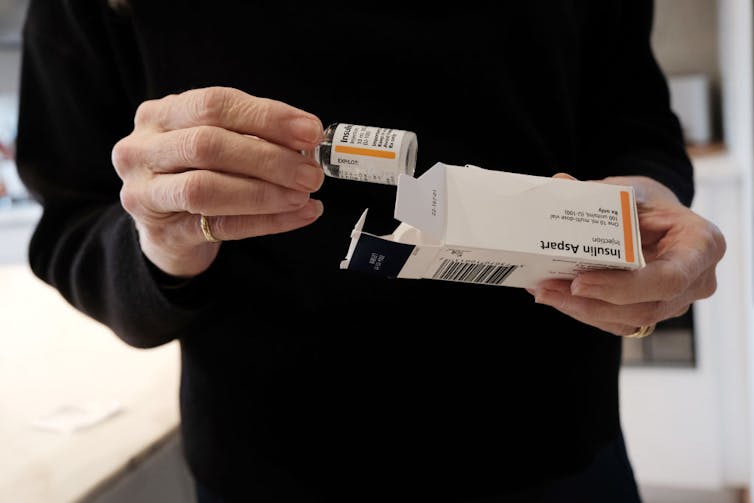 Person holding taking vial of insulin out of box