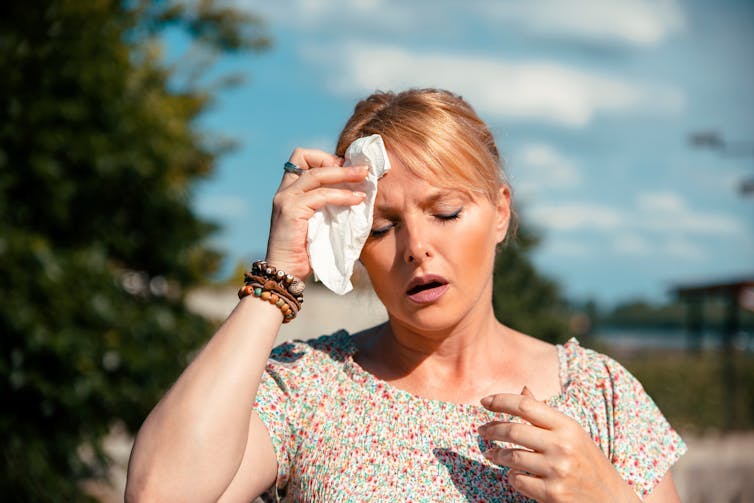 A woman dabs her forehead with a tissue to remove sweat.