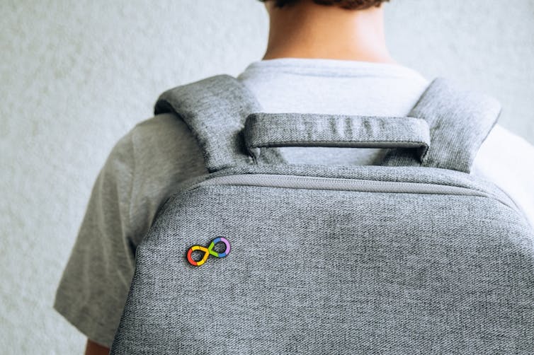 A grey backpack with the neurodivergent symbol (an infinity sign in rainbow colours) pinned to it.