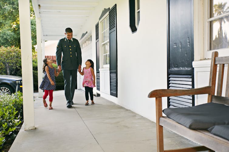 Solder in uniform walks hand in hand with two young girls, one on each side, looking up at him.