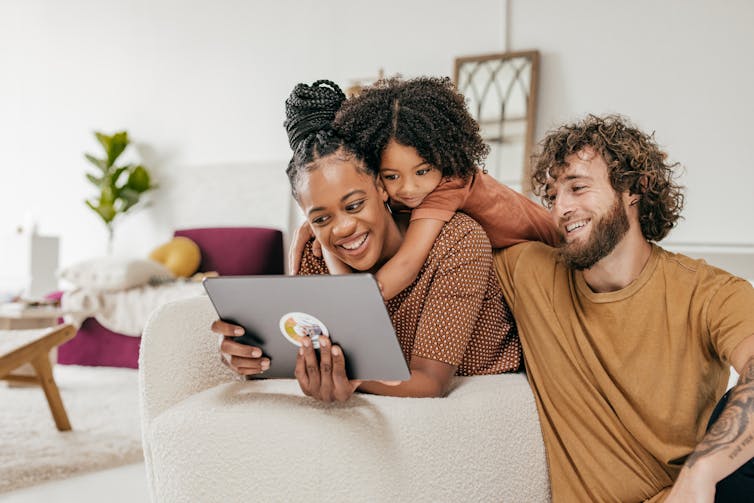 A woman, man and child look at a tablet screen in a living room