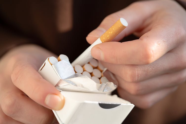 Close up of a pair of hands pulling a cigarette out of a pack