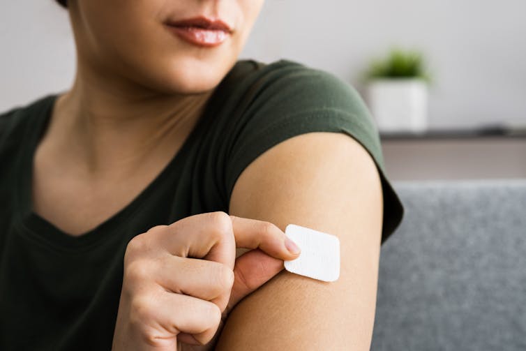 A woman applies an HRT patch to her upper arm.