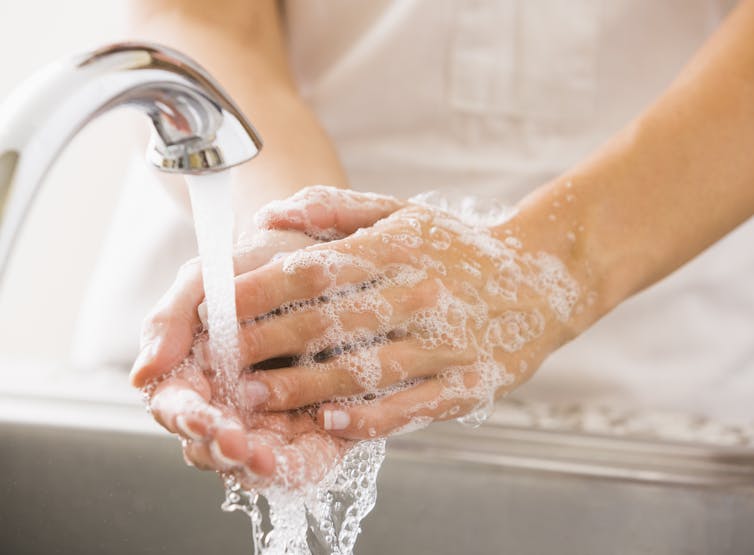 Person's hands covered with suds under a running faucet.